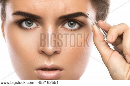 Close-up Of Female Face And Eyebrow With Tweezers