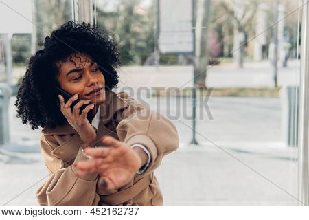 Front View Of An Adult Woman Hailing Taxi Cab On The Street While Talking On Phone With Copy Space.