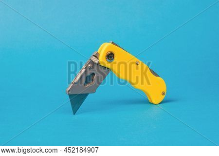 Folding Knife For Cutting Paper And Cardboard On A Blue Background. Reliable Hand Tool For Cutting.