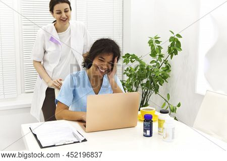 Portrait Of Two Beautiful Young Female Mixed Race Doctors By Laptop While Smiling In Hospital Having