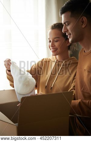 Excited Young Couple Unpacking Box With Appliences They Ordered For New Kitchen