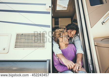 Happy Adult Couple Enjoy Happiness Sitting On The Door Of Their Camper Van Mobile Home.  Concept Of 