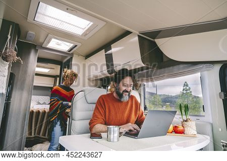 Daily Normal Life Inside A Camper Van Rv Mobile Home. Woman Cooking In The Kitchen And Adult Man Wor