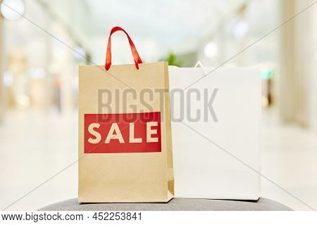 Background Image Of Paper Shopping Bags With Red Sale Word In Shopping Mall Interior, Copy Space