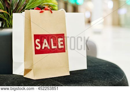 Background Image Of Paper Shopping Bags With Red Sale Word On Velvet Couch In Shopping Mall, Copy Sp