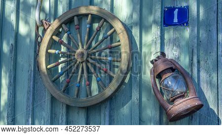 Betty Lamp And Spinning Wheel In The Background Of The Old Log-house Wall With Sign Nomber One. Rura