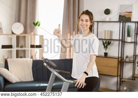 Young Caucasian Woman With Fitness Bracelet Doing Cardio Exercies On A Treadmill At Home. Modern Hom