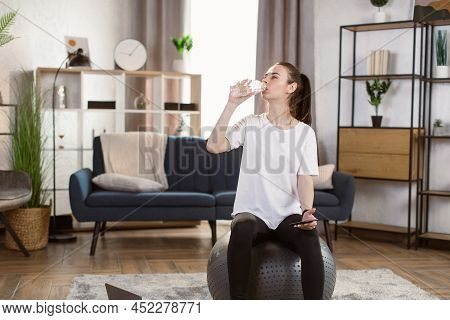 Young Caucasian Woman In Black Sports Leggings And A White T-shirt With Smart Phone Sitting On Fit B
