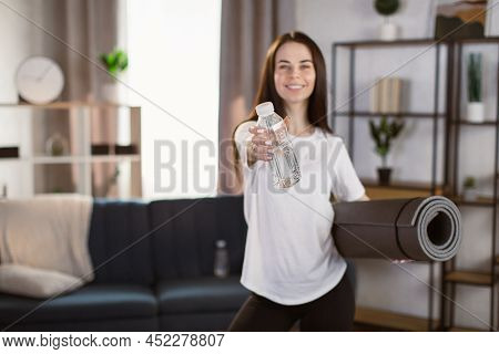 Focus On A Bottle With Water In Hand Of Beautiful Caucasian Woman In Leggings And A White T-shirt. T