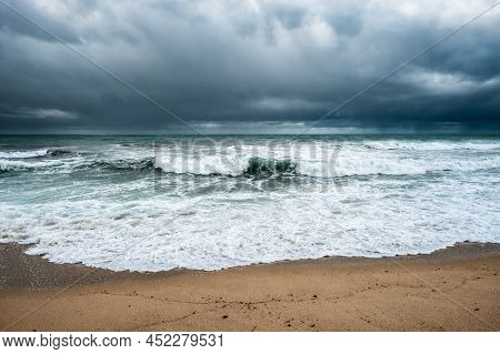 Rough Seas Crash Onto The Beach At Algajola In The Balagne Region Of Corsica With Dark Clouds And Ra