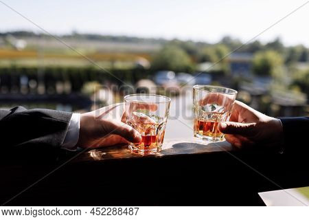 Close Up Of Two Hands Of Men In Suits With Glasses Of Whiskey Drink Outdoors. Alcoholic Beverage. Hi