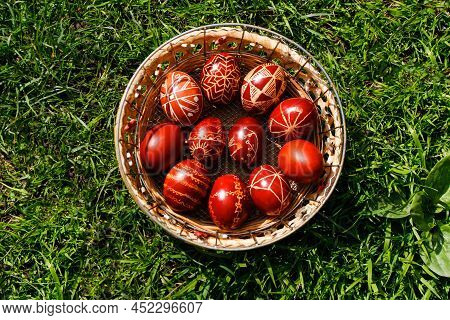 Defocus Closeup Of Basket Of Colored Red Eggs On Nature Green Grass Background. Easter Holiday Conce