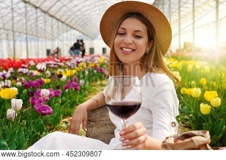 Relaxed Beautiful Woman Enjoying A Glass Of Red Wine Between Tulips On Spring Time