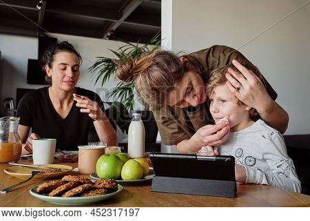 Young Lesbian Family Having Breakfast With Their Adopted Child At Table At Home