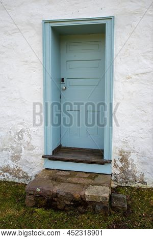 Quaint And Charming Closed Light Blue Door With Stone Staps In A Whitewashed Weathered Stone Cottage