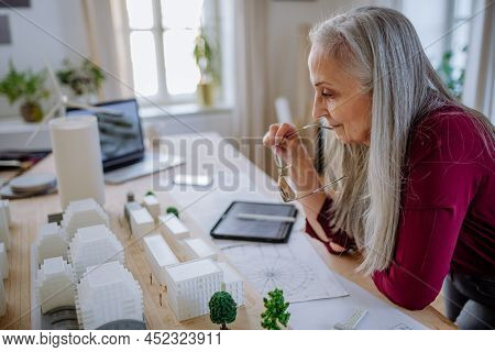 Senior Woman Eco Architect With Model Of Modern Bulidings Working In Office.