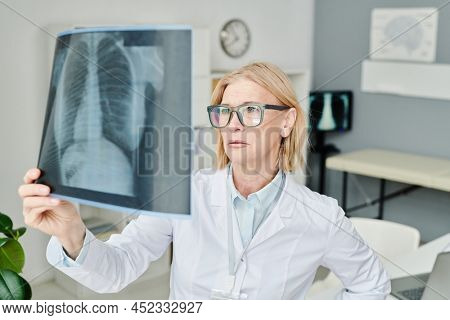 Mature experienced radiologist in whitecoat looking at rontgen of lungs while trying to establish exact diagnosis of patient