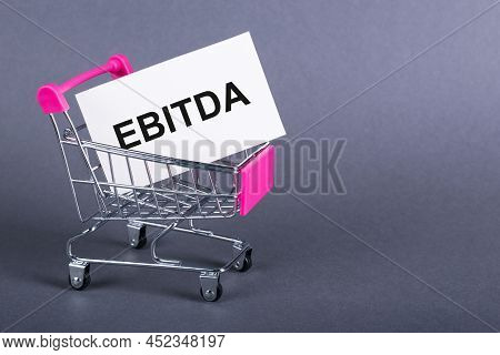 On A Gray Background, A Shopping Cart, A Card With The Word Ebitda.