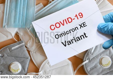 Doctor's Hand In Blue Glove With White Paper And Text Covid-19 Omicron Xe Variant With Various Prote