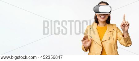 Image Of Young Asian Woman Wearng Vr Headset, Using Virtual Reality Glasses And Smiling, Pointing At