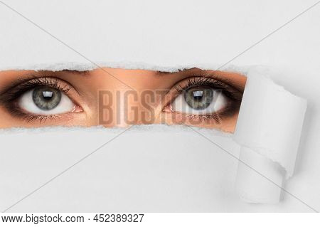 Young Female Eyes Looking Through Torn Paper
