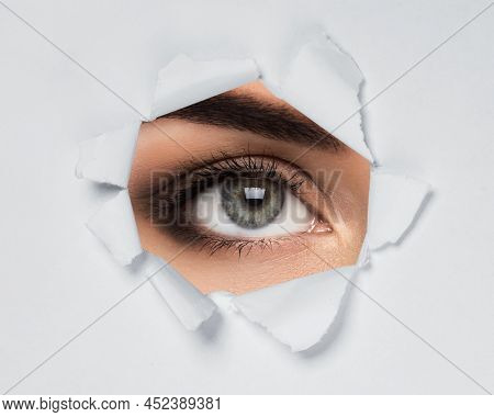 Young Female Eye Looking Through Torn Paper