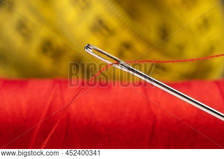 Eye Of The Needle With Red Polyester Thread. Spool Of Red Polyester Sewing Thread. Measuring Tape In