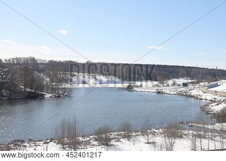 Sunny April Day On The Shore Of The Lake. Bare Branches Of Bushes And Birches. Blue Sky.