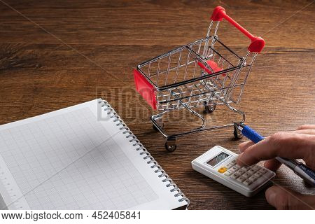 Man Calculates The Budget. Shopping Cart A On Table With Calculator And Paper. Budget Of Poor And Lo