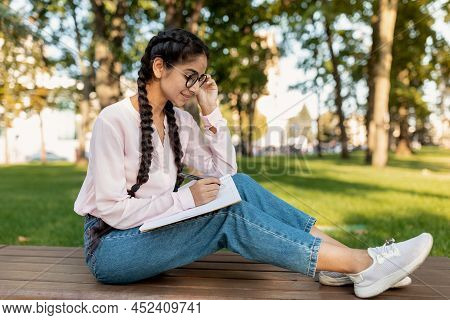 Happy Indian Female Student Sketching While Sitting On Bench In Park Outdoors, Free Space. Studentsh