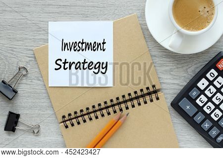 Investment Strategy. Text On White Sticker On Notepad And Wood Background