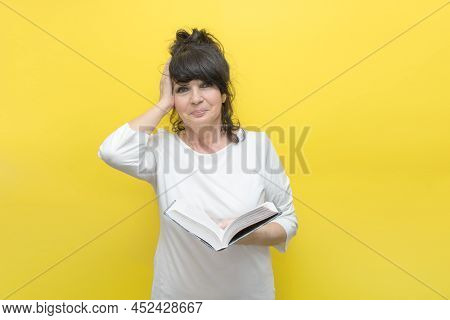 Sympathetic Elderly Woman Holds A Book In Her Hand, Clutches Her Head In Emotions From What Is Writt