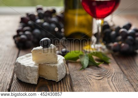 Camember Cheese With Dark Grapes And Red Wine On Wooden Table In Summer Day.