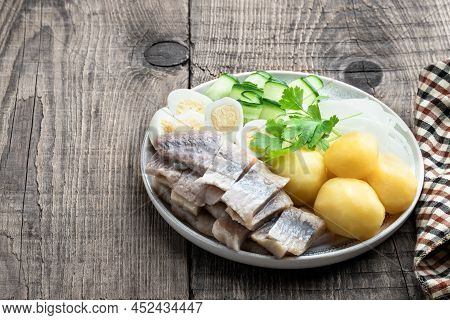 Salted  Herring With Boiled Potatoes And Quial Eggs On A White Plate On Wooden Table