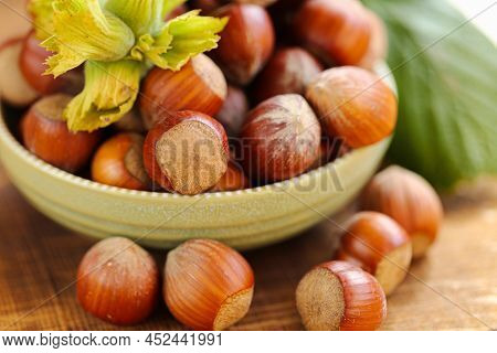 Hazelnuts Close-up In A Green Cup On A Wooden Table. Whole Nuts With Green Leaves. Harvest Of Hazeln