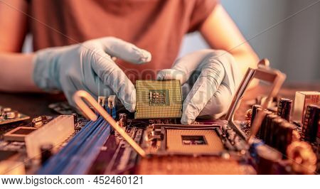 The Engineer's Gloved Hand Is Holding The Cpu Chip Against The Background Of The Motherboard. Concep