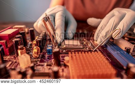 The Engineer's Gloved Hand Is Holding The Cpu Chip Against The Background Of The Motherboard. Concep