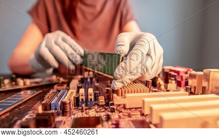 The Engineer's Gloved Hand Holds The Computer's Ram Chip Against The Background Of The Motherboard. 