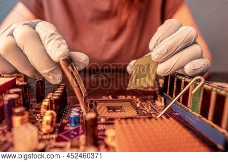 The Engineer's Gloved Hand Is Holding The Cpu Chip Against The Background Of The Motherboard. Concep