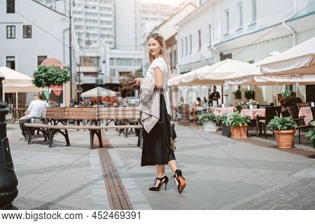 Ashionable Woman With A Smartphone Walking Along A City Street.