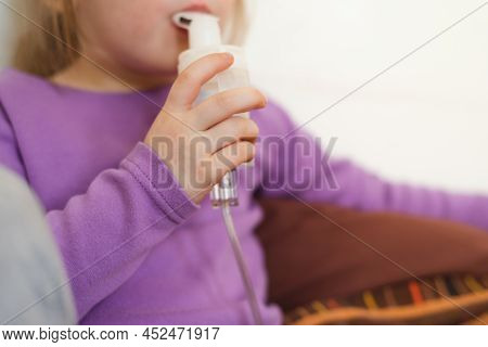 Sick Child Lies In Bed And Makes Inhalation Using A Nebulizer. Close-up Of A Child's Hand With A Neb