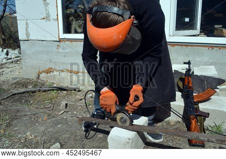 Man working in the garden with grinder. Russian assault rifle AK-74 standing next to him. April 7, 2022. Kiev Region, Ukraine