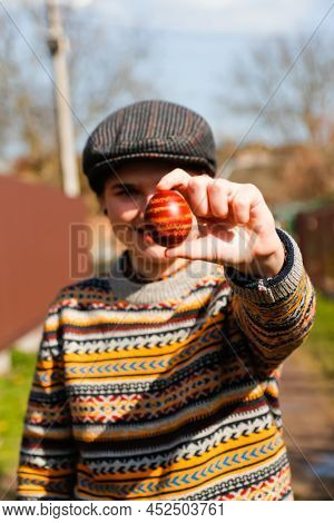 Defocus Ukrainian Young Woman In Hat Holding One Colored Red Egg On Nature Background. Easter, Ukrai
