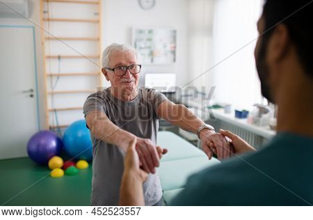 Young Physiotherapist Exercising With Senior Patient In A Physic Room