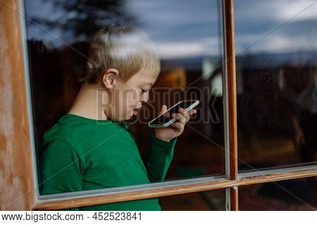 Sad Little Boy With Down Syndrome Using Smartphone At Home