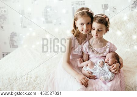 Two Little Sisters With Their Newborn Brot