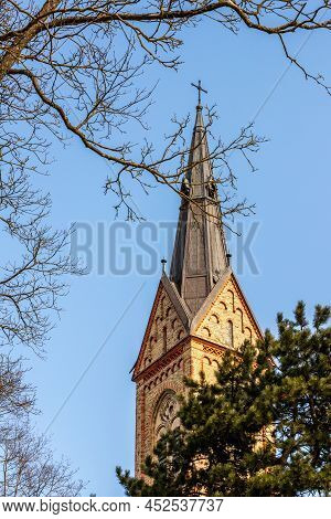 Vertical View To Yellow Rock Church Tower With Metal Roof With Green Pine Tree And Leafless Spring B