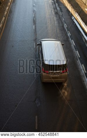 Toyota Alphard 350g Driving Along The Street, Aerial View. Rear Top View Of Dirty Minivan In Motion 