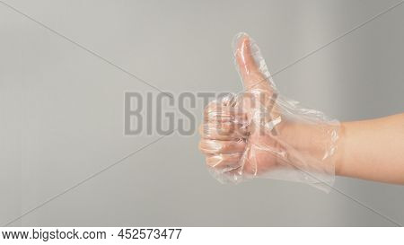 The Hand Is Wearing A Disposable Plastic Glove And Do Like Handsign On Grey Background.