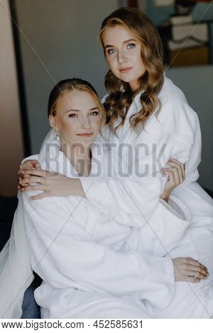 Young Beautiful Models Are Sitting On The Bed In White Bathrobes And Looking